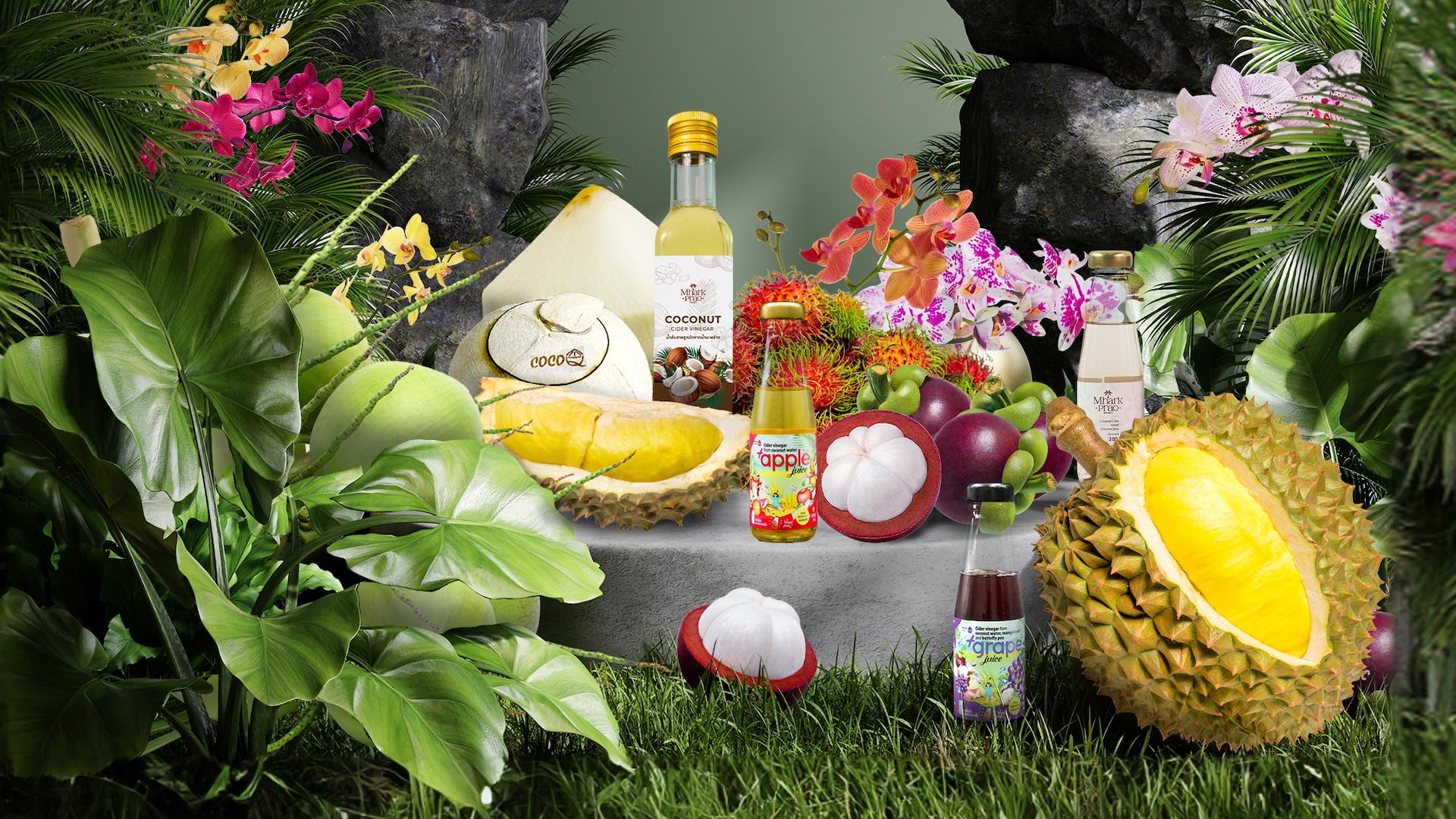 The image showcases a vibrant still life arrangement featuring various tropical fruits, bottles of juice, and lush green foliage. The composition highlights the fruits and juices with artistic lighting, suggesting a focus on natural products.